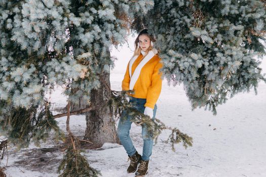 Teen blonde in a yellow sweater outside in winter. A teenage girl on a walk in winter clothes in a snowy forest.