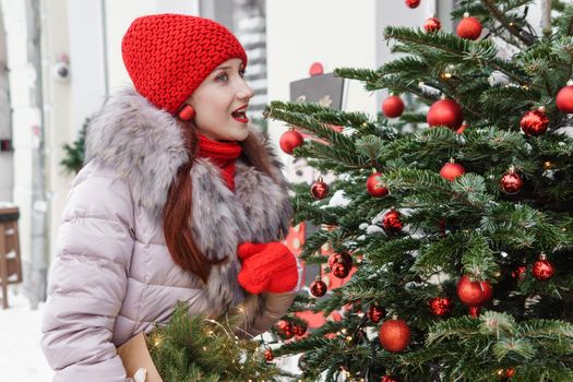 A bright woman in winter clothes walks around the city decorated for Christmas. Lifestyle in the winter season.