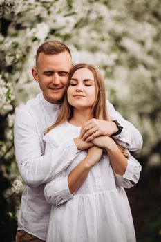 Young loving couple in a walk in a spring blooming apple orchard. Happy married couple enjoy each other while walking in the garden. Man holding woman's hand