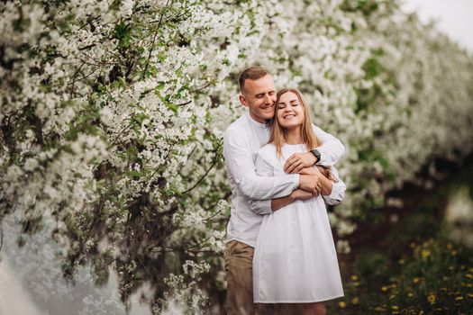 Young loving couple in a walk in a spring blooming apple orchard. Happy married couple enjoy each other while walking in the garden. Man holding woman's hand