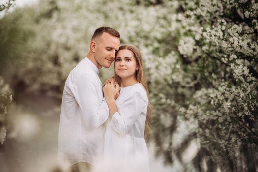 Young loving couple in a walk in a spring blooming apple orchard. Happy married couple enjoy each other while walking in the garden. Man holding woman's hand