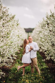 Beautiful young couple in a romantic place, spring blooming apple orchard. Happy joyful couple enjoy each other while walking in the garden. Man holding woman's hand