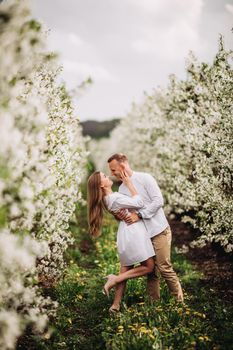 Beautiful young couple in a romantic place, spring blooming apple orchard. Happy joyful couple enjoy each other while walking in the garden. Man holding woman's hand