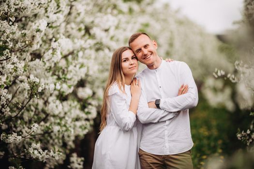 Young loving couple in a walk in a spring blooming apple orchard. Happy married couple enjoy each other while walking in the garden. Man holding woman's hand