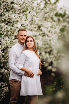 Young loving couple in a walk in a spring blooming apple orchard. Happy married couple enjoy each other while walking in the garden. Man holding woman's hand