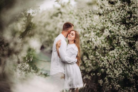 Happy family couple in love in a spring blooming apple orchard. Happy family enjoy each other while walking in the garden. The man holds the woman's hand. Family relationships