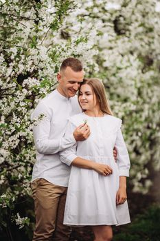 Happy family couple in love in a spring blooming apple orchard. Happy family enjoy each other while walking in the garden. The man holds the woman's hand. Family relationships