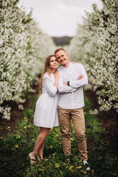 Beautiful young couple in a romantic place, spring blooming apple orchard. Happy joyful couple enjoy each other while walking in the garden. Man holding woman's hand