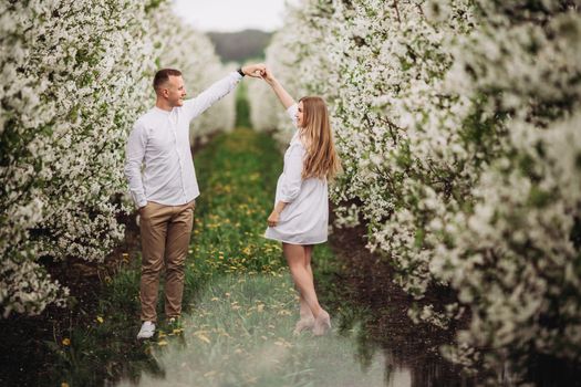 Happy family couple in spring blooming apple orchard. Young couple in love enjoy each other while walking in the garden. The man holds the woman's hand. Family relationships