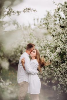 Happy family couple in love in a spring blooming apple orchard. Happy family enjoy each other while walking in the garden. The man holds the woman's hand. Family relationships