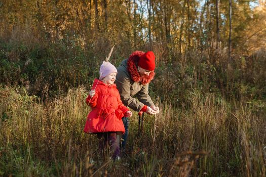 A little girl in a red coat walks in nature in an autumn grove with her grandmother. The time of the year is autumn