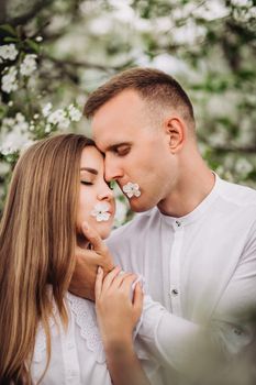 Young loving couple in a walk in a spring blooming apple orchard. Happy married couple enjoy each other while walking in the garden. Man holding woman's hand