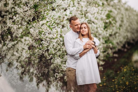 Happy family couple in love in a spring blooming apple orchard. Happy family enjoy each other while walking in the garden. The man holds the woman's hand. Family relationships