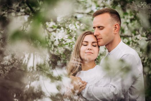 Happy family couple in love in a spring blooming apple orchard. Happy family enjoy each other while walking in the garden. The man holds the woman's hand. Family relationships