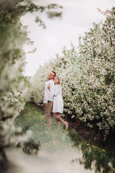 Happy family couple in spring blooming apple orchard. Young couple in love enjoy each other while walking in the garden. The man holds the woman's hand. Family relationships