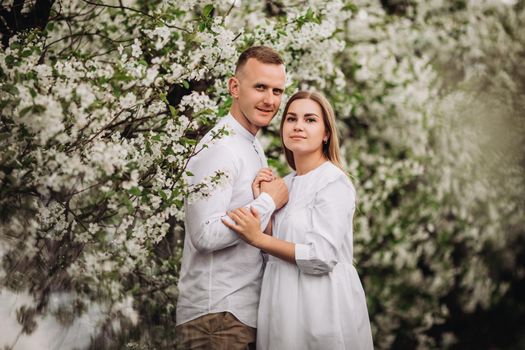 Happy family couple in love in a spring blooming apple orchard. Happy family enjoy each other while walking in the garden. The man holds the woman's hand. Family relationships