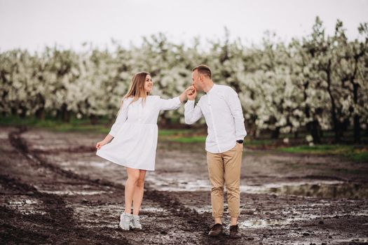 Happy family couple in the spring blooming apple orchard. Young couple in love enjoy each other while walking in the garden. Mud underfoot. The man holds the woman's hand. Family relationships
