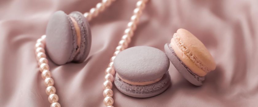 Girly, bakery and branding concept - Sweet macaroons and pearls jewellery on silk background, parisian chic jewelry, French dessert food and cake macaron for luxury confectionery brand, holiday gift