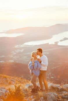 Man hugs a woman from behind and kisses her temple while standing on a mountain above the bay. High quality photo