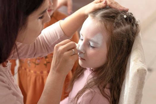 selective focus. A makeup artist works. childrens makeup face paint drawings Girls face painting. Little girl having face painted on birthday party. closed eyes. aqua make-up