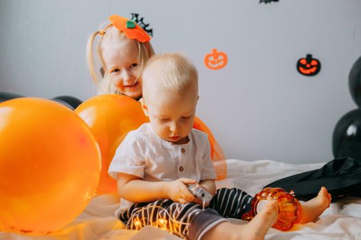 Children's Halloween - a boy and a girl in carnival costumes with orange and black balloons at home. Ready to celebrate Halloween.