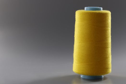 Yellow bobbin of thin threads on a gray background, close-up. Tailoring and repair of clothes, machine embroidery