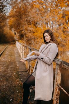 A beautiful long-haired woman walks through the autumn streets. Railway, autumn leaves, a woman in a light coat.