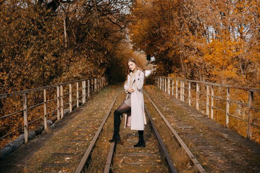 A beautiful long-haired woman walks through the autumn streets. Railway, autumn leaves, a woman in a light coat.