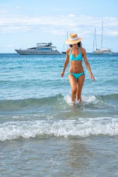 Woman with turquoise bikini and hat posing on a beach in Ibiza