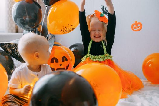 Children's Halloween - a boy and a girl in carnival costumes with orange and black balloons at home. Ready to celebrate Halloween.