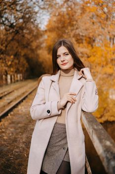 A beautiful long-haired woman walks through the autumn streets. Railway, autumn leaves, a woman in a light coat.