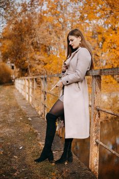 A beautiful long-haired woman walks through the autumn streets. Railway, autumn leaves, a woman in a light coat.