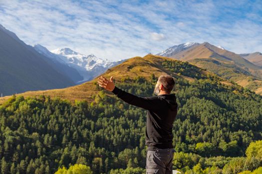 A man stands on top of a mountain with his arms outstretched