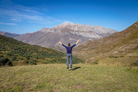 An adult man stands on top of a mountain with outstretched arms
