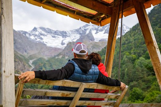 A man and a woman swing on a swing high in the mountains. Relax and enjoy nature