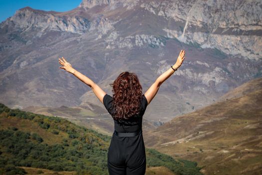 A young woman stands on top of a mountain with her arms outstretched