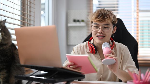 Man sitting front of laptop and using microphone to recording audio in home studio. Mass media, technology and people concept.