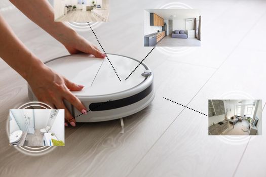 happy young woman using smart home application on smartphone and robot vacuum cleaning floor in background in the modern living room