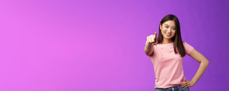 We need you our team. Friendly good-looking outgoing asian woman brunette pointing camera, indicate index finger, smiling motivated, picking person, making decision, stand purple background.