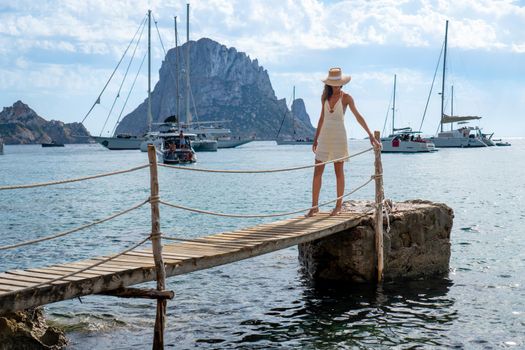 Brunette woman with hat and light beige dress on Ibiza pier