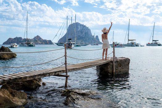 Brunette woman with hat and light beige dress on Ibiza pier