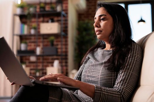 Business woman sitting on couch and working, doing remote office job on laptop pc at home. Using computer to work on data report, sending email and browsing internet for research plan.