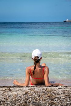 Brunette woman with coral bikini and cap posing on the beach