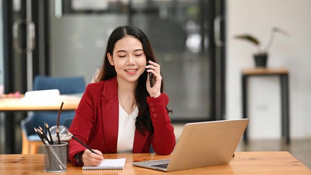 Attractive asian businesswoman talking on mobile phone and working with laptop computer.