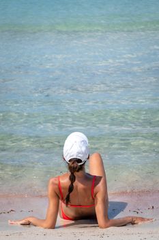 Brunette woman with coral bikini and cap posing on the beach