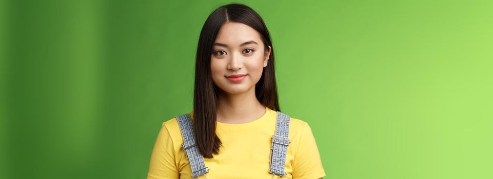 Waist-up friendly cheerful teenage asian college girl stand green background, smiling lovely, look tender amused, have relaxing casual conversation, packing things summer journey. Copy space