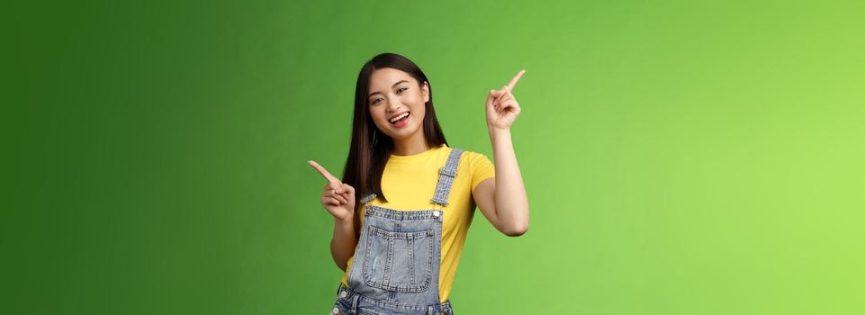 Friendly stylish good-looking upbeat teenage asian brunette, dancing joyfully showing few choices, shopping online easy picking products, pointing sideways left right, smiling enthusiastic.