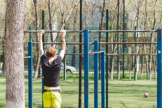 Sports. A man is engaged in a horizontal bar. Outdoor pull-ups. Sports complex in the open air.