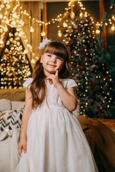 A girl in a festive light dress next to a Christmas tree, lights of garlands in the background. The concept of New Year holidays.
