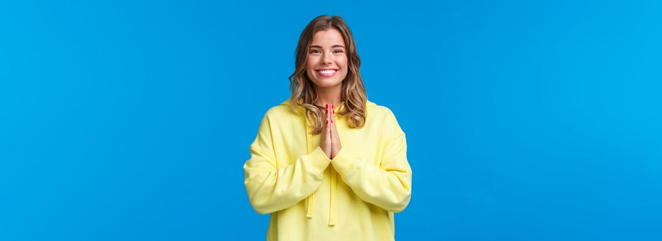 Cheerful young european female practice yoga, greeting sensei with namaste gesture, hold hands in pray and smiling grateful with relaxed carefree expression, smiling camera, blue background.